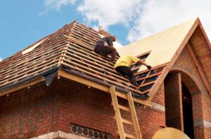 Inspector checking shingles and flashing on a residential roof with a clipboard in hand.