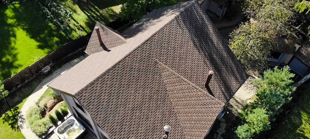 Two adults inspecting a residential roof and reviewing paperwork together on a sunny day.